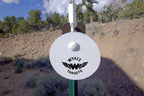 6-inch white AR500 gong hanging on a T-post hanger at the range