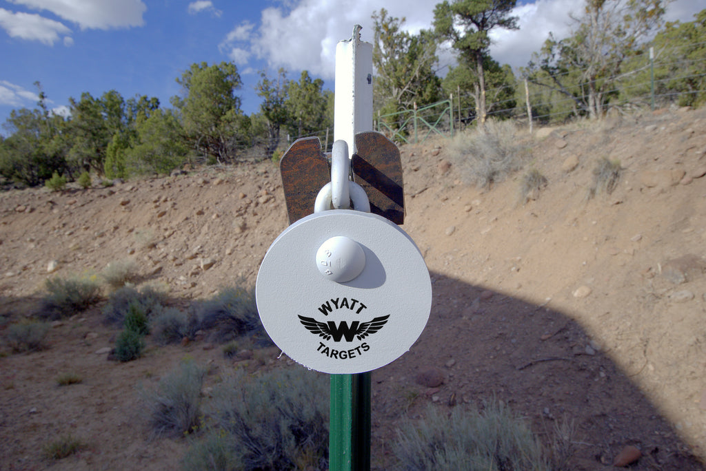 4-inch white AR500 gong hanging on a T-post hanger at the range