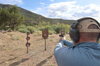 Real photo: shooter firing a pistol at Wyatt Surface Rust AR500 steel targets in factory red-oxide primer, hanging on T-posts at the range