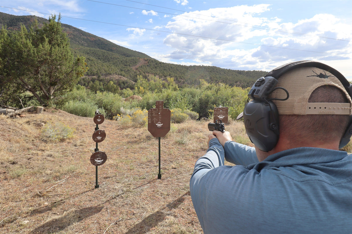 Real photo: shooter firing a pistol at Wyatt Surface Rust AR500 steel targets in factory red-oxide primer, hanging on T-posts at the range
